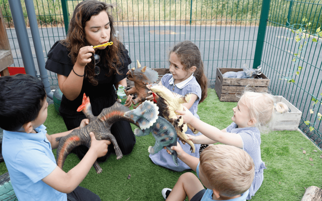 Starting Pre-School at Cheadle Hulme Primary School. Children gather around a member of staff who blows bubbles in the outdoor learning area.